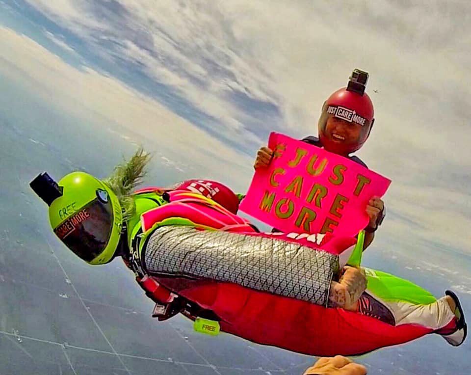 Jamie Leibert and Sandra Zinovyev in freefall holding a Just Care More sign, Captain Manicorn and Ladycorn on mission