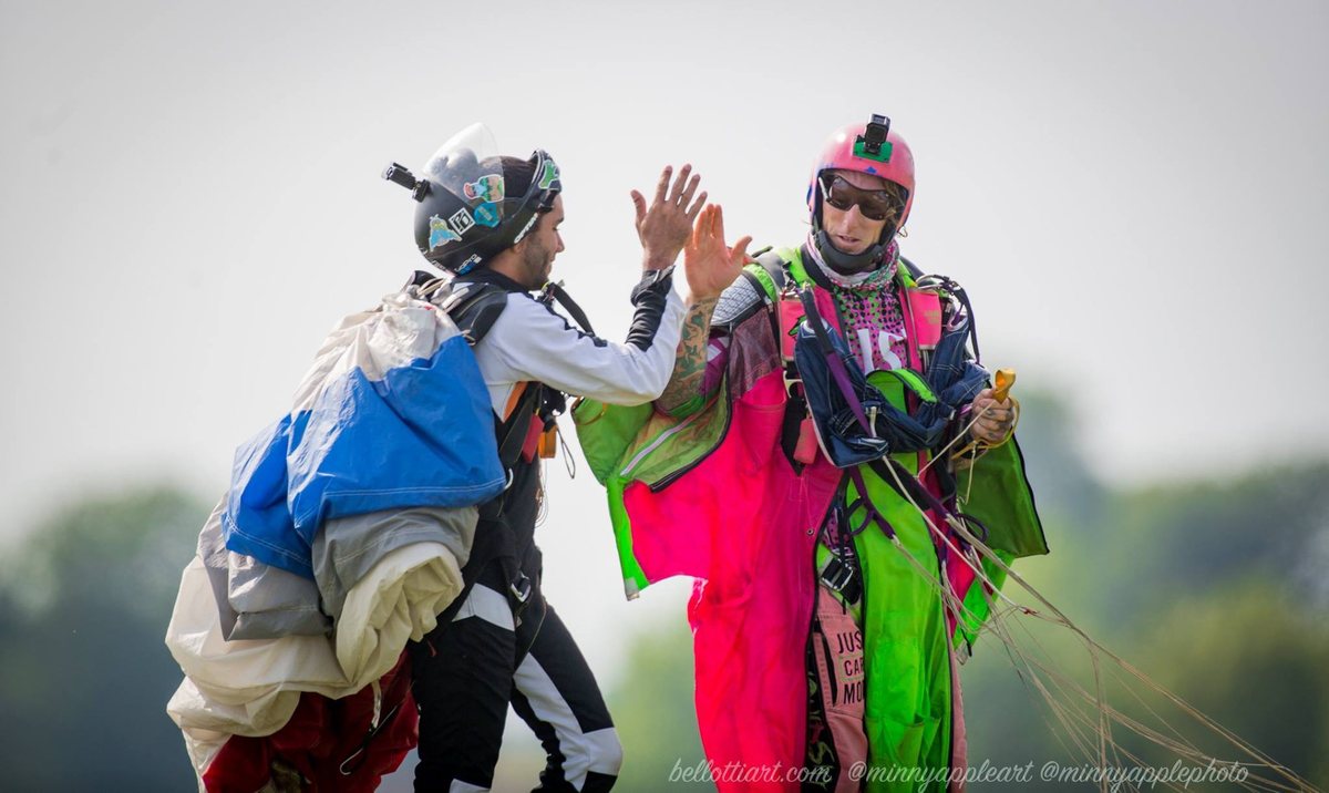 Jamie Leibert in his Just Care More wingsuit after landing, greeted by a fellow jumper, professional adventure athlete and founder of Battling Monsters